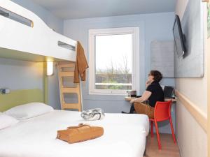 a woman sitting at a desk in a bedroom with a bunk bed at ibis budget Paris Porte de Vanves in Vanves