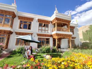 uma mulher sentada debaixo de um guarda-chuva em frente a um edifício em Namra Villa em Leh