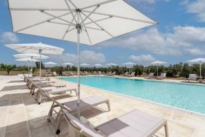einen Pool mit Tischen, Stühlen und einem Sonnenschirm in der Unterkunft Palummare - Agri Hotel Relais in Torre San Giovanni Ugento