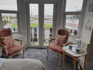 Zimmer mit 2 Stühlen, einem Tisch und Fenstern in der Unterkunft Henrys on the Prom in Great Yarmouth