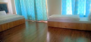 Habitación con 2 camas, suelo de madera y cortinas azules. en Zee Guest House, en Leh