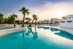 a swimming pool with palm trees and a building at Pareus Beach Resort in Caorle