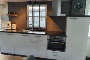 een keuken met witte kasten, een wastafel en een klok bij Vazonics Valkenbosch 76 in Oisterwijk