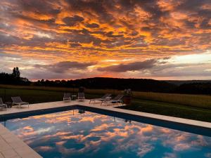 a swimming pool with a sunset in the sky at Domaine de Cazal - Chambres d'Hôtes avec piscine au cœur de 26 hectares de nature préservée in Saint-Cyprien