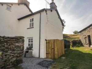Casa blanca con puerta de madera y pared de piedra en Crag End Cottage en Grange Over Sands