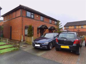 Deux voitures garées sur un parking en face d'une maison dans l'établissement BRIGSTOCK HOLIDAYS HOUSE, à Manchester
