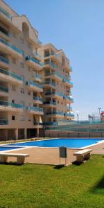 ein großes Apartmenthaus mit einem Pool und zwei Bänken in der Unterkunft Apartamento Blau Mar in Piles
