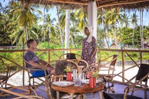 Ein Mann und eine Frau sitzen an einem Tisch auf einer Veranda. in der Unterkunft Heart of Zanzibar Bungalows in Paje