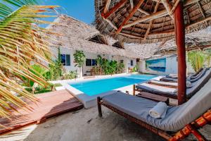 an outdoor swimming pool with chaise lounge chairs and an umbrella at King Simba Apartment Hotel in Bwejuu
