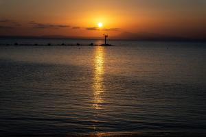 a sunset over the ocean with a lighthouse in the water at Tylos Beach Hotel in Kato Pyrgos