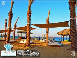 a beach with palm trees and a beach umbrella at Apartment in Blue bay Asian Marsailla Families only chalet pool view قرية بلو باى اسيا مرسيليا العين السخنة in Ain Sokhna