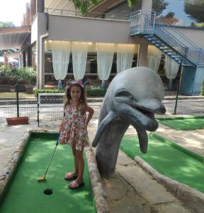 a little girl standing next to a dolphin playing golf at Hotel Shipka Beach in Sunny Beach