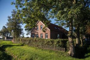 a red brick house with a fence and a tree at Moderne Unterkunft Landzeit Esens nahe der Nordsee - ökologisch saniertes Ferienhaus in Esens