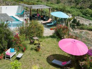 un jardin avec un parasol et des chaises roses ainsi qu'une piscine dans l'établissement Casa Turquesa 25 Minuten vom Strand, à Guájar Fondón
