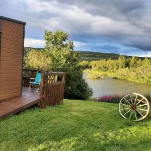 eine Holzterrasse mit einem Stuhl auf dem Gras neben einem Fluss in der Unterkunft Hagi 1 Guesthouse in Aðaldalur