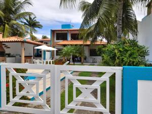 a white fence in front of a house with palm trees at Casa de praia aconchegante em Sonho Verde in Paripueira