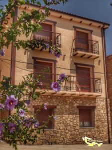 un edificio de piedra con balcones y flores púrpuras en Apartamentos El Arenal, en Acebo
