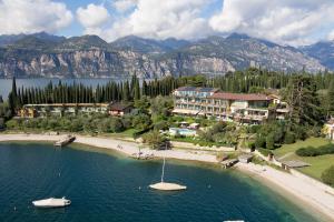 a beach with a resort and a boat in the water at Hotel Maximilian in Malcesine