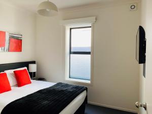 Un dormitorio con una cama con almohadas rojas y una ventana en 315 Euro Motel and Serviced Apartments, en Dunedin