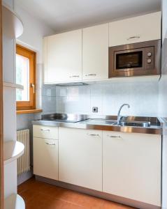 a kitchen with white cabinets and a sink and a microwave at Apartments Lores in Selva di Val Gardena