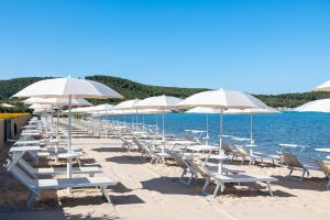 a row of white chairs and umbrellas on a beach at Hotel Corte Rosada in Porto Conte +37 photos