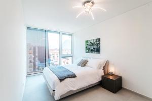 a white bedroom with a bed and a large window at Flat Iron Apartments by Quokka 360 - modern building 5 min from the centre of Lugano in Viganello
