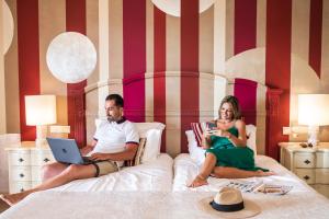 a man and a woman sitting on a bed with a laptop at Boutique Hotel Vivenda Miranda in Lagos