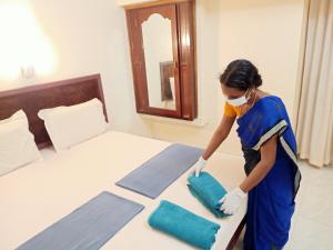 a woman in a mask putting pillows on a bed at Marina guest house in Kovalam