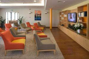 - une salle d'attente avec des chaises orange et gris et une télévision dans l'établissement Domitys Les Clés d'Or, à Orthez