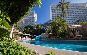 a pool at a hotel with palm trees and buildings at Emporio Acapulco in Acapulco