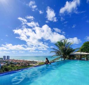 a woman sitting in a infinity pool with a view of the ocean at Pousada Paradise Vista do Atlantico in Maceió