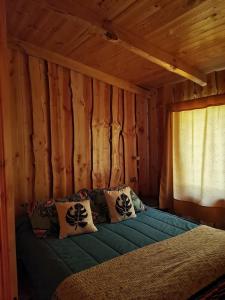 a bed in a log cabin with a window at Cabaña GAROVE in Panguipulli