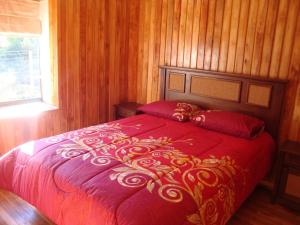 Una cama roja en una habitación con paredes de madera. en Cabañas Maroni, en Las Trancas