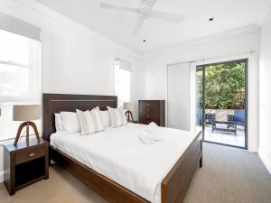 a white bedroom with a large bed and a balcony at Neptune Hyams Beach in Hyams Beach