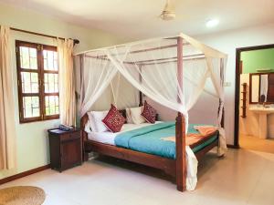 een slaapkamer met een hemelbed in een kamer bij Flame Tree Cottages in Nungwi