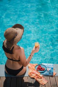 a woman in a hat holding a drink next to a pool at Avilia Suites in Fethiye