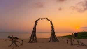 een houten boog op het strand met de zonsondergang op de achtergrond bij ザ・ビーチテラスホテルアオ石垣 in Ishigaki Island