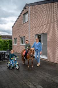 Eine Frau und zwei Kinder und eine Frau auf einem Pferd und einem Fahrrad in der Unterkunft Hoevetoerisme Op 't Zand in Neerpelt