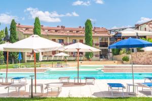 a pool with umbrellas and tables and chairs next to a building at Hotel Palazzuolo in San Quirico dʼOrcia