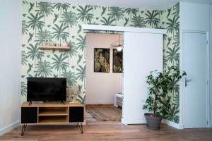 a living room with a tv on a cabinet and palm wallpaper at ONLOC - Appart Réveil proche Halles avec parking in Pau