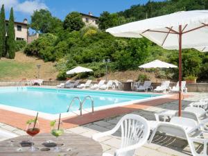 a swimming pool with white chairs and an umbrella at Apartment Vigna La Corte-5 by Interhome in Dicomano