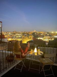 a woman sitting at a table with a view of a city at Douro Virtudes Apartments Historical Center in Porto