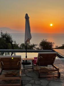 路特奇的住宿－SEA BREEZE STUDIO，露台上的遮阳伞和两把椅子享有日落美景
