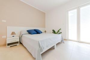 una camera bianca con un letto con cuscini blu sopra di Case Vacanza Apollo a Torre San Giovanni Ugento