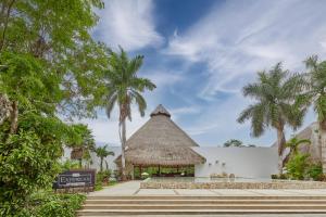 a building with a thatched roof and palm trees at The Explorean Kohunlich - All Inclusive in Ruinas Kohunlích