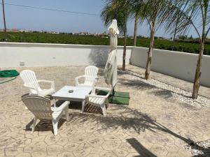 eine Terrasse mit weißen Stühlen, einem Tisch und einem Sonnenschirm in der Unterkunft Case Vacanze Giovanna in Petrosino