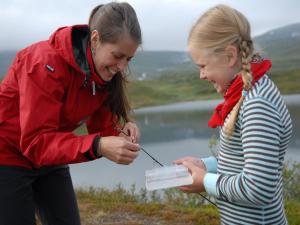 two women standing on a mountain looking at a device at Hotell Fjället in Björkliden