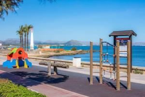 Un parque con una zona de juegos infantiles con el océano al fondo. en House by the sea in Can Picafort with terrace, en Can Picafort