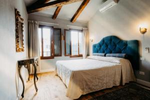 a bedroom with a bed with a blue headboard and windows at Palazzo Veneziano direct at the canal with roof terrace in Venice