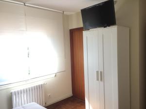 una camera da letto con TV sopra un armadio bianco di Pensión Avenida a O Pedrouzo